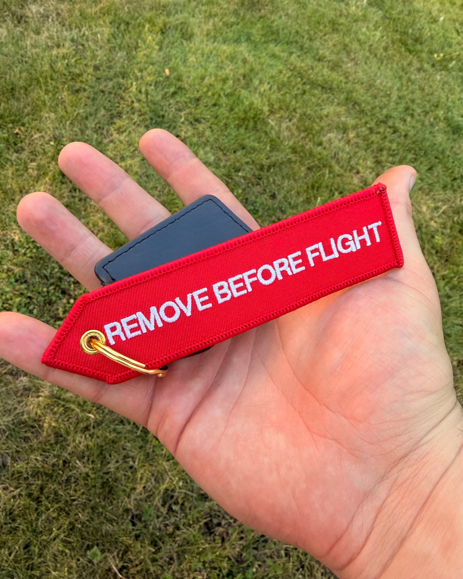 Roter "Remove before Flight" Schlüsselanhänger mit goldenem Ring in der Hand gehalten
