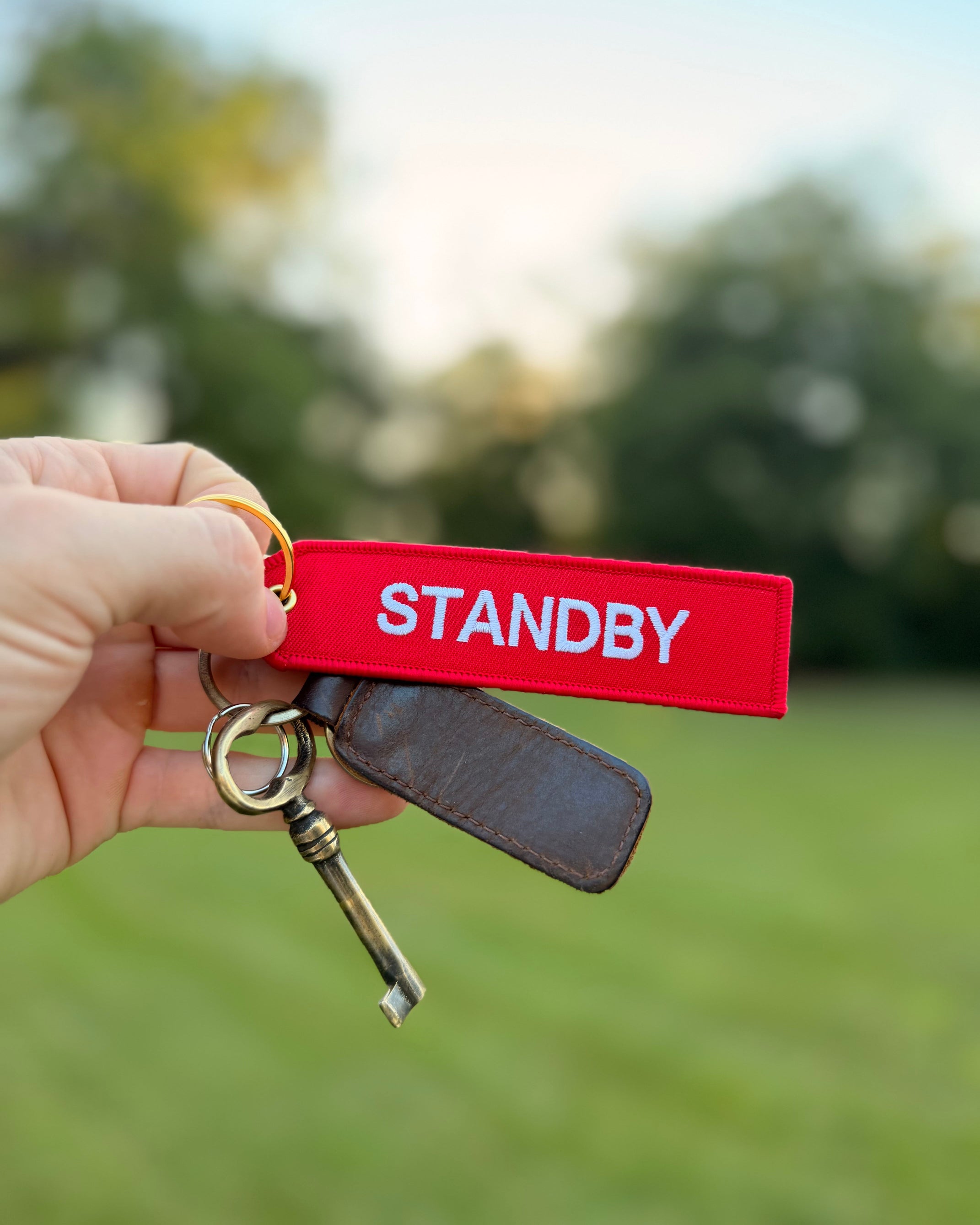 Roter „Standby“ Schlüsselanhänger mit weißer Stickerei und goldfarbenem Ring am Schlüsselbund