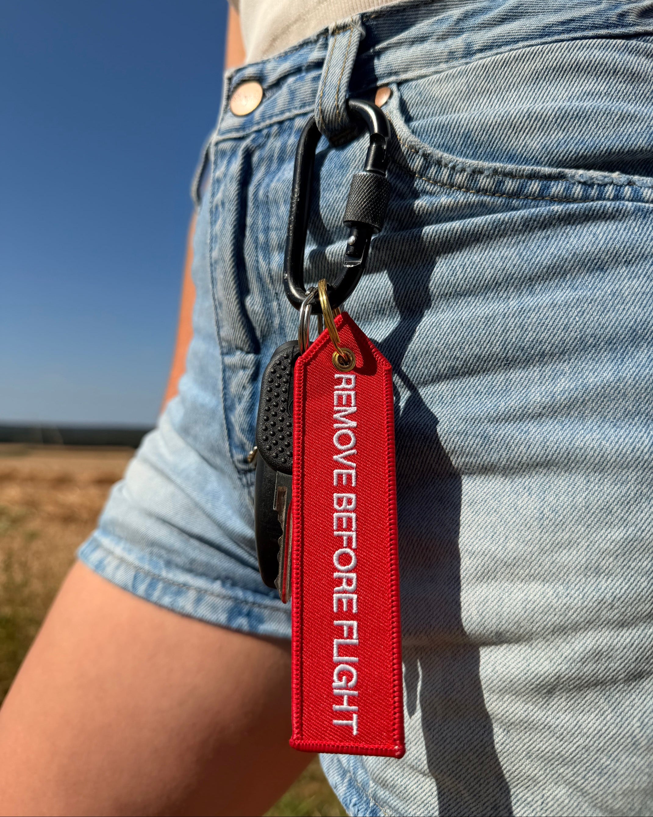 Roter "Remove before Flight" Schlüsselanhänger mit goldenem Ring am Hosenbund mit Karabinerhaken