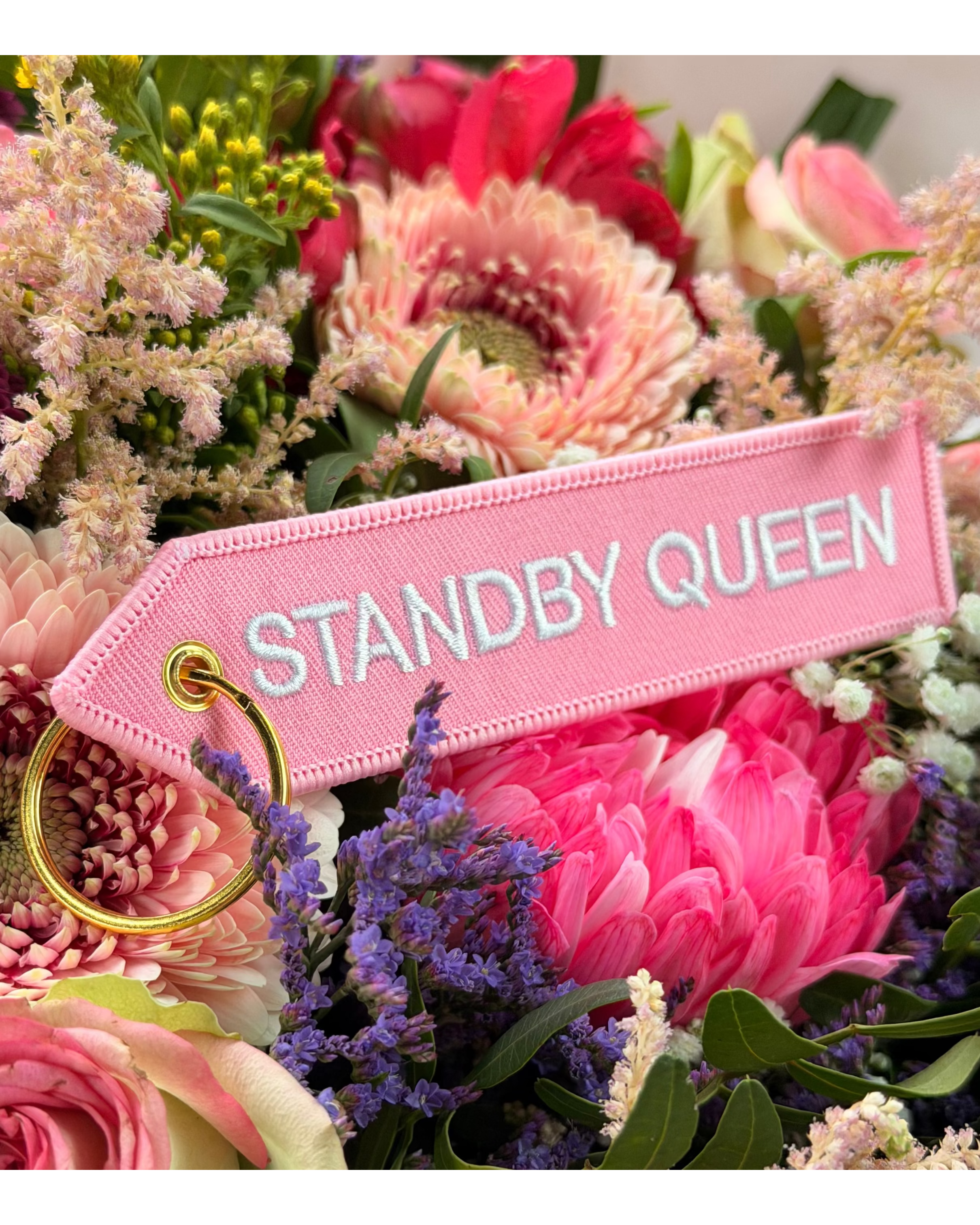Rosa Schlüsselanhänger Standby Queen vor buntem Blumenstrauss mit goldenem Ring